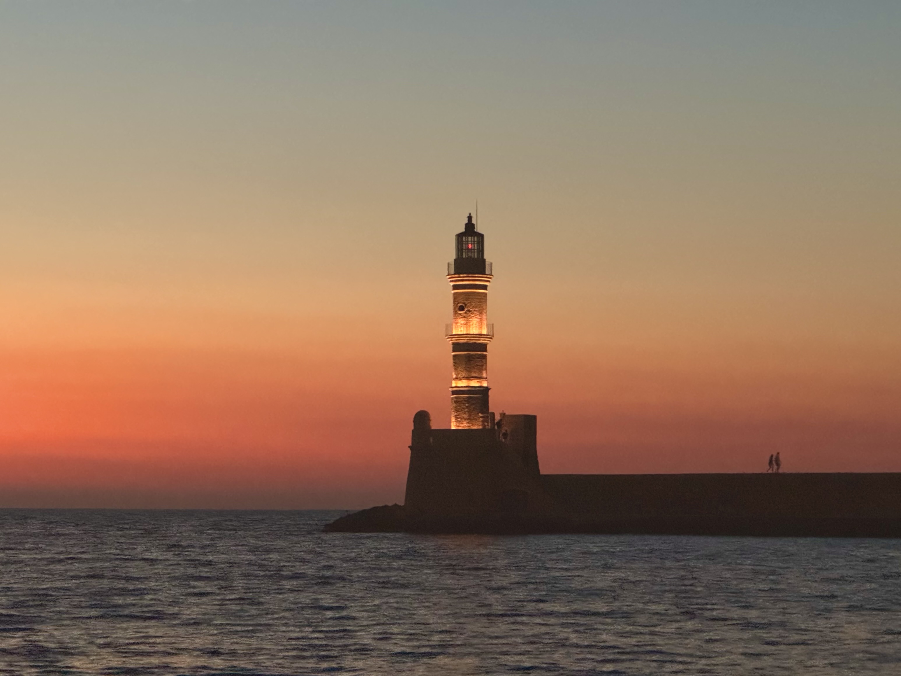 A lighthouse silhouetted against an orange sunset over the harbor in Chania, Crete